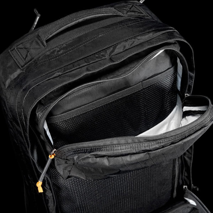 The GR2 X-PAC backpack in black features AquaGuard zippers, a mesh pocket, and a zippered compartment, displayed against a black background.