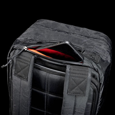 The GR2 X-PAC, a black backpack with AquaGuard zippers, is shown against a black background with a phone partly tucked into its zippered pocket.