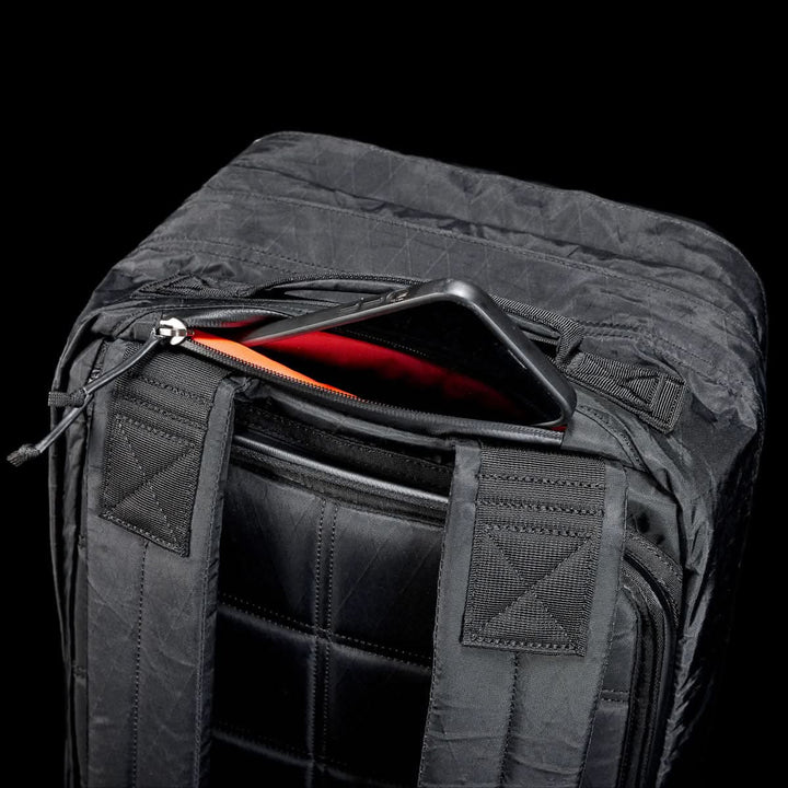 The GR2 X-PAC, a black backpack with AquaGuard zippers, is shown against a black background with a phone partly tucked into its zippered pocket.