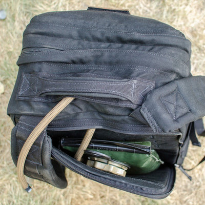 Open GR2 USA Throwback backpack on grass, revealing green packets and goggles inside the main compartment—crafted from rugged 1000D Cordura for durability.