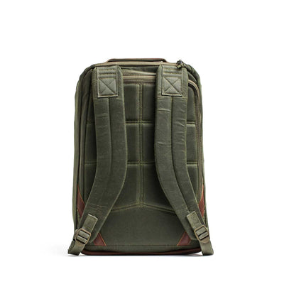 The GR1 USA - Heritage Waxed Canvas backpack in olive green is shown from the back, with padded straps, brown leather accents, and classic waxed canvas rucksack styling.