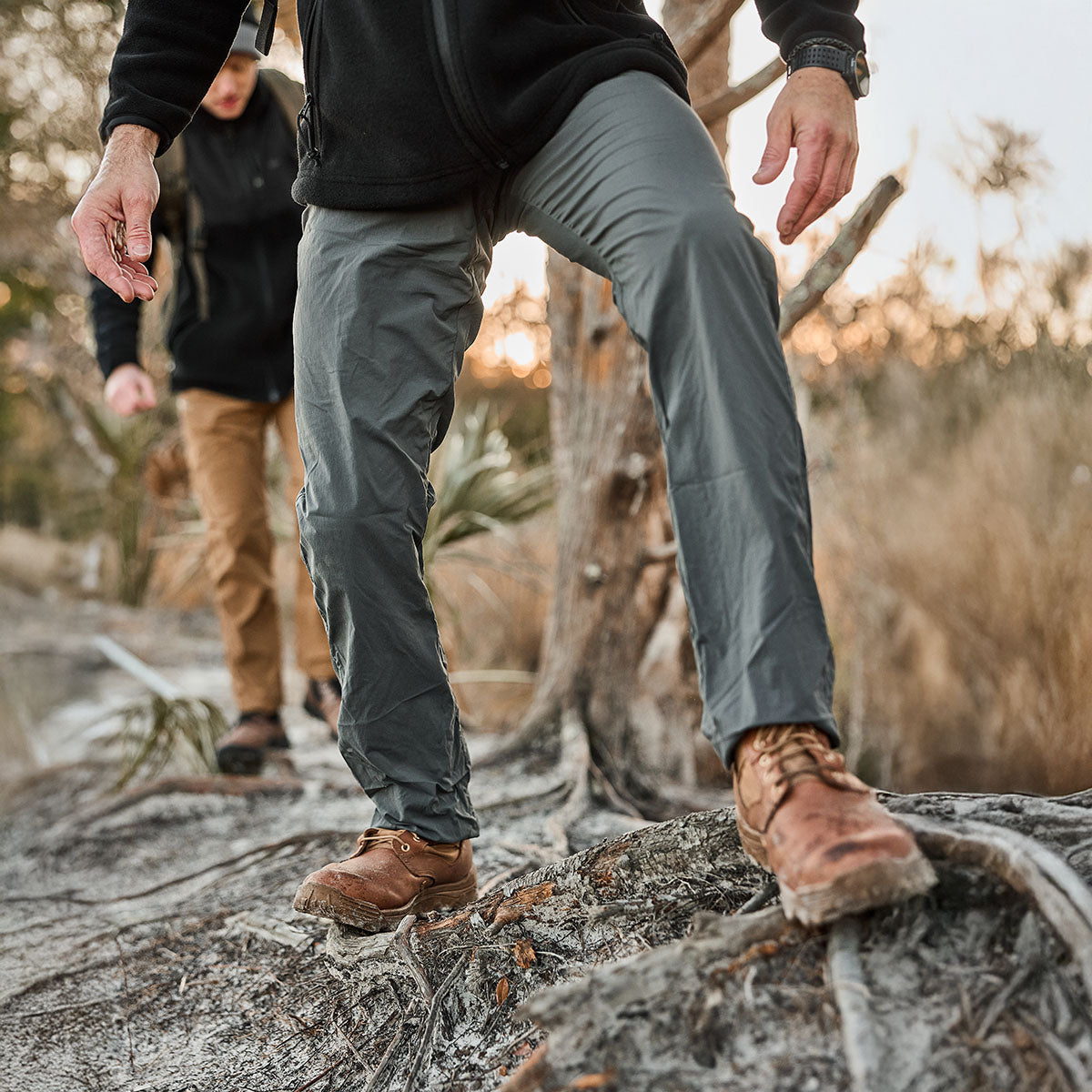 Two people hiking on a forest trail, sporting reliable boots and outdoor clothing. The person in front stands out wearing Men’s Simple Pants - Midweight ToughDry®, designed for comfort and adventure-ready resilience.