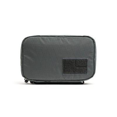 The GR1 Field Pocket USA - X-PAC is a rectangular gray pouch with a black front patch, ideal as a travel accessory and shown against a white background.