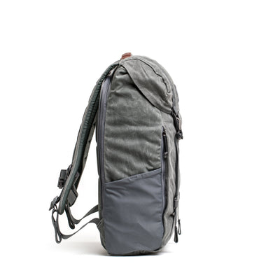 The gray GORUCK M24 waxed canvas rucksack features side pockets and extra padded shoulder straps, shown upright on a white background.