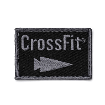 A rectangular black patch bordered in gray features the word CrossFit in bold gray text, with a distinct gray triangle pointing to the right below it, capturing the GORUCK style. This product is known as Patch - GORUCK x CrossFit from GORUCK-DEMO.