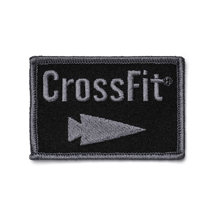 A rectangular black patch bordered in gray features the word CrossFit in bold gray text, with a distinct gray triangle pointing to the right below it, capturing the GORUCK style. This product is known as Patch - GORUCK x CrossFit from GORUCK-DEMO.