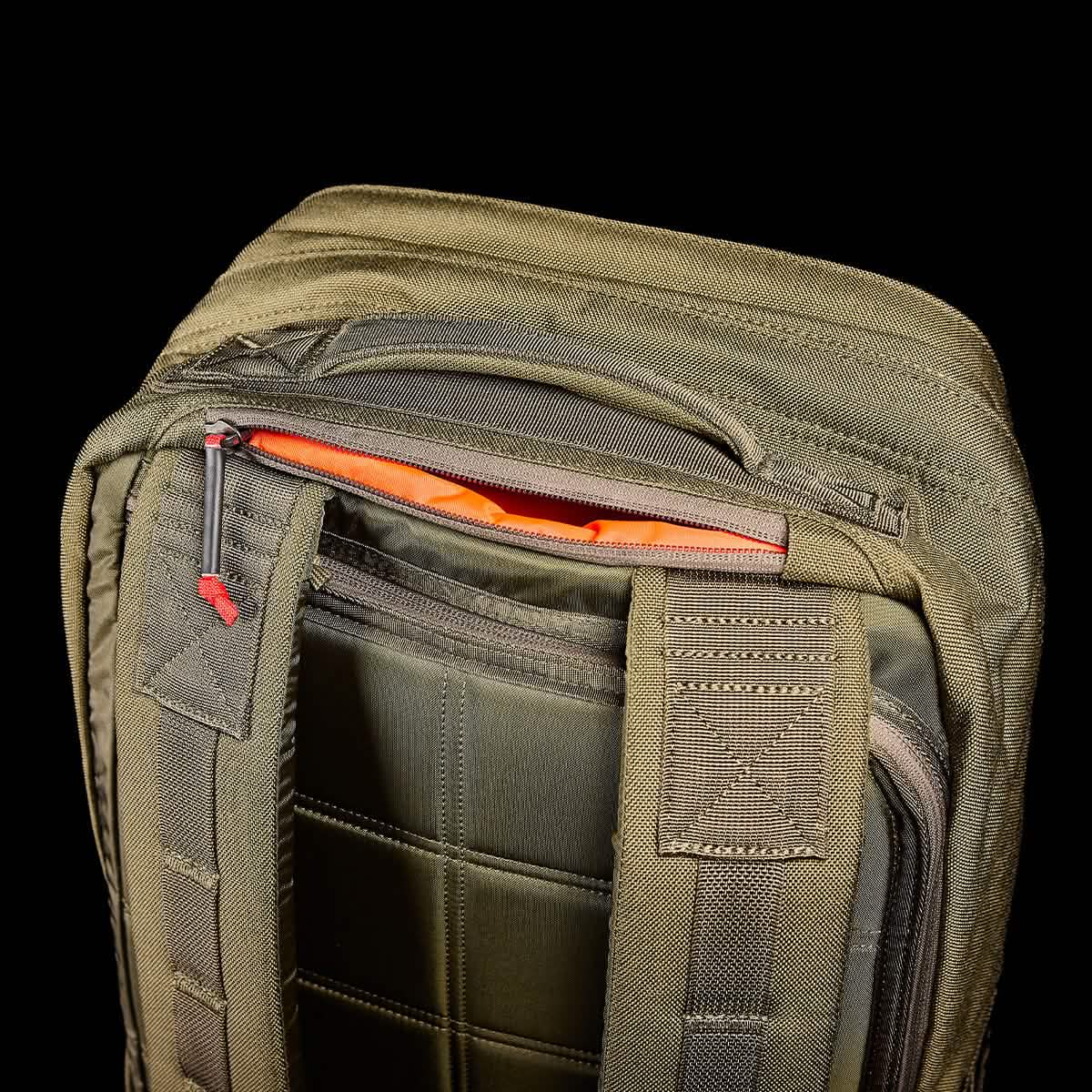 Close-up of the olive green GR2 backpack from GORUCK, showcasing its partially open top zipper that reveals an orange interior. Crafted with Special Forces quality in mind, this backpack boasts sturdy stitching and padded straps for enhanced durability. Set against a black background, its details are highlighted, making it ideal for carry-on compliant travel.