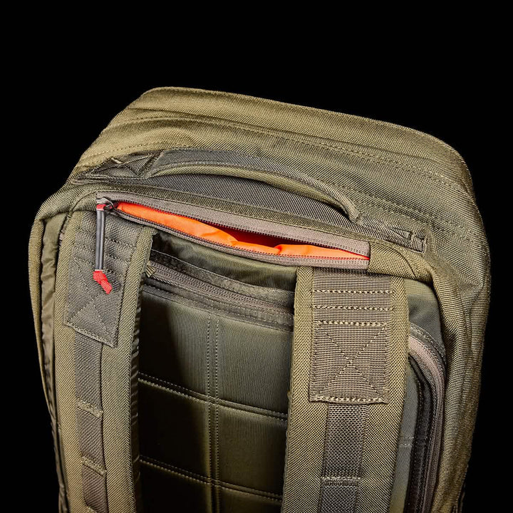 Close-up of the olive green GR2 backpack from GORUCK, showcasing its partially open top zipper that reveals an orange interior. Crafted with Special Forces quality in mind, this backpack boasts sturdy stitching and padded straps for enhanced durability. Set against a black background, its details are highlighted, making it ideal for carry-on compliant travel.