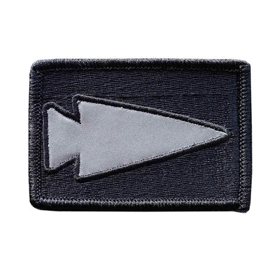 Introducing the GORUCK Patch - Reflective Spearhead: This rectangular black patch showcases an embroidered gray spearhead symbol centered on the patch, oriented to the left. It is designed with a stitched border and equipped with a VELCRO backing for effortless attachment.