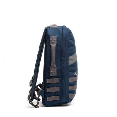 Side view of the Rucker 4.0, a blue rucksack with gray straps and webbing, standing upright on a white background—ideal for rucking or carrying ruck plates.