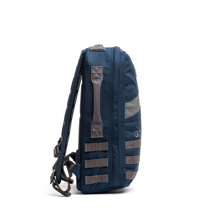 Side view of the Rucker 4.0, a blue rucksack with gray straps and webbing, standing upright on a white background—ideal for rucking or carrying ruck plates.