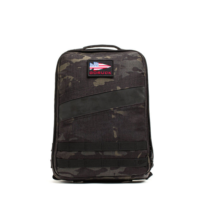 The Rucker 4.0 is a black camo rucksack featuring a top handle and an American flag patch labeled "GORUCK"—ideal for rucking or hauling your Ruck Plates.