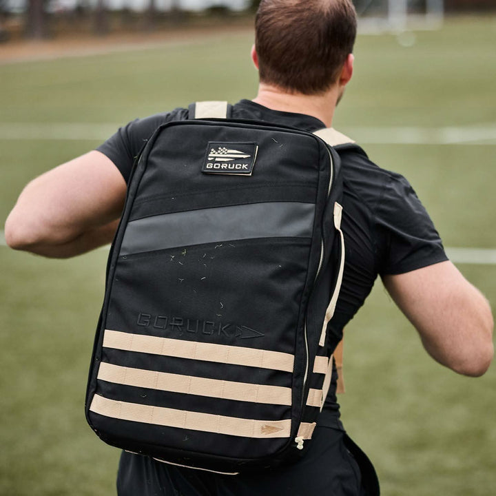 A person with a GORUCK Rucker 4.0 in black and beige, designed for rucking, jogging across a grassy field.