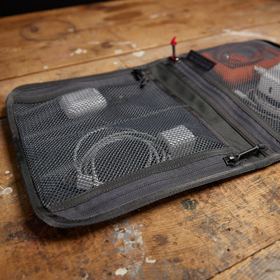 The Wire Dopp, made from tough CORDURA mesh, keeps your electronic accessories organized for travel essentials and is neatly displayed on a wooden surface.