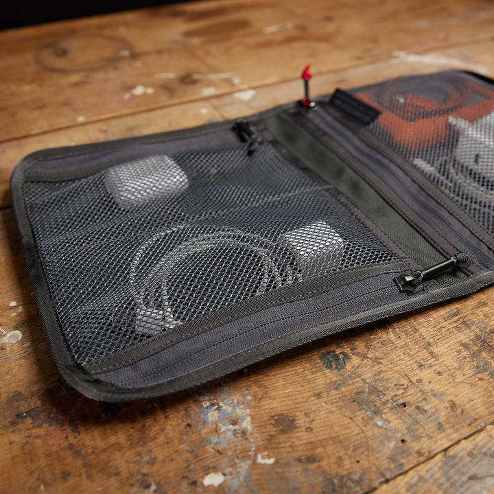 The Wire Dopp, made from tough CORDURA mesh, keeps your electronic accessories organized for travel essentials and is neatly displayed on a wooden surface.