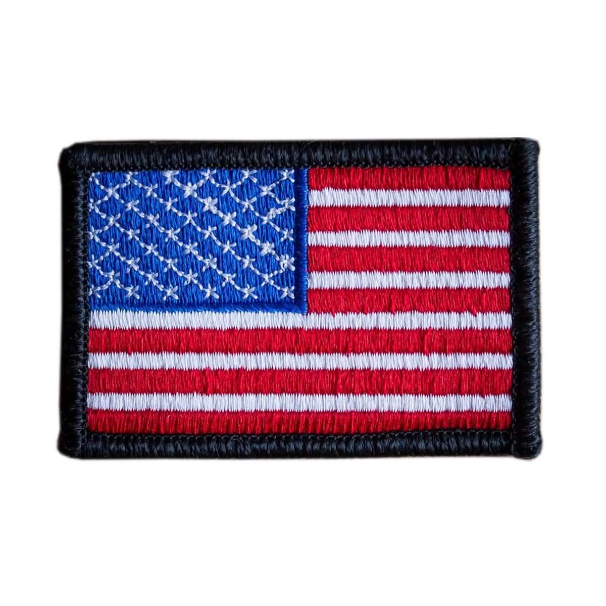 The "Patch - American Flag" by vendor-unknown is an embroidered patch showcasing the United States flag design. It features red and white stripes with a blue rectangle in the top left corner adorned with white stars, all bordered in black, and comes with a VELCRO® backing for effortless attachment.