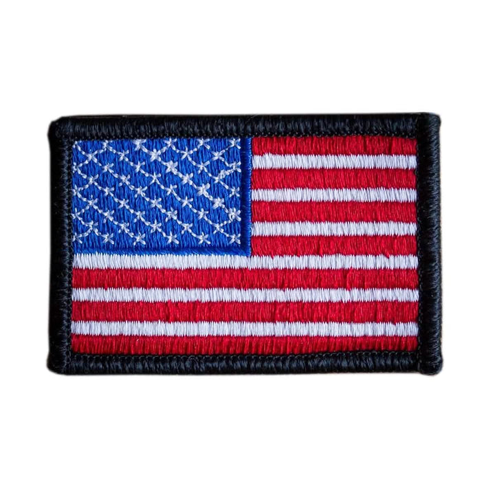 The "Patch - American Flag" by vendor-unknown is an embroidered patch showcasing the United States flag design. It features red and white stripes with a blue rectangle in the top left corner adorned with white stars, all bordered in black, and comes with a VELCRO® backing for effortless attachment.