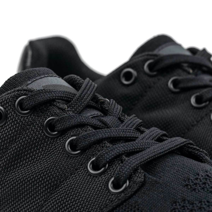 Close-up of the Men's Ballistic Trainers - Blackout w/ Black Reflective Spearhead by GORUCK, showcasing a pair of black athletic shoes made with CORDURA® Ballistic Nylon. These shoes feature textured fabric and black laces with metal eyelets, designed for functional fitness footwear. They offer a sleek, modern look complemented by durable 3X Support™ for enhanced performance.