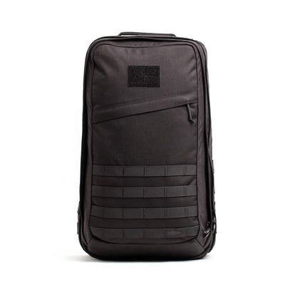 The GORUCK GR2 is a sleek black backpack with a minimalist rectangular design and a zippered front pocket. Ideal for travel, it features horizontal MOLLE straps at the bottom and a small patch area at the top, reminiscent of Special Forces style.