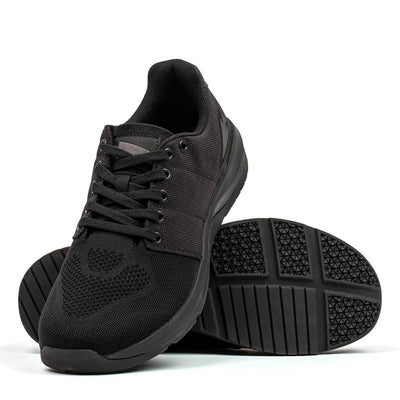 Introducing the Men's Ballistic Trainers in Blackout with Black Reflective Spearhead by GORUCK, designed for functional fitness enthusiasts. These athletic shoes feature a mesh design and durable CORDURA® Ballistic Nylon. One shoe stands upright, showcasing the sleek look, while the other leans to reveal a textured sole pattern enhanced by 3X Support™ technology.