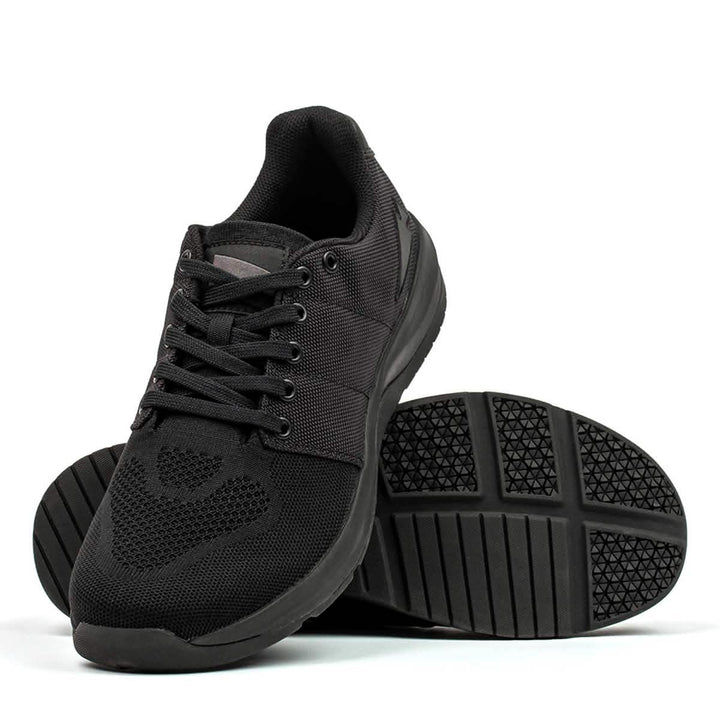 Introducing the Men's Ballistic Trainers in Blackout with Black Reflective Spearhead by GORUCK, designed for functional fitness enthusiasts. These athletic shoes feature a mesh design and durable CORDURA® Ballistic Nylon. One shoe stands upright, showcasing the sleek look, while the other leans to reveal a textured sole pattern enhanced by 3X Support™ technology.
