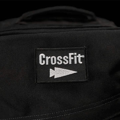 A close-up view of the Patch - GORUCK x CrossFit from GORUCK-DEMO showcases the word 'CrossFit' and a stylized arrow logo in white. The patch is stitched onto a black fabric surface, likely part of a bag or clothing item, with a dark and out-of-focus background.