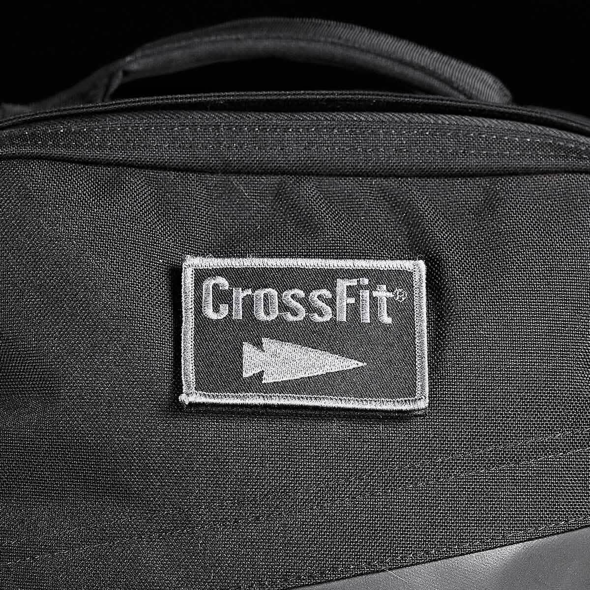 A black fabric bag prominently displays a rectangular patch embroidered with the CrossFit logo and an arrow symbol in white. The stitching accentuates the central patch, seamlessly merging durability with style, embodying the rugged design principles of GORUCK-DEMO's Patch - GORUCK x CrossFit.