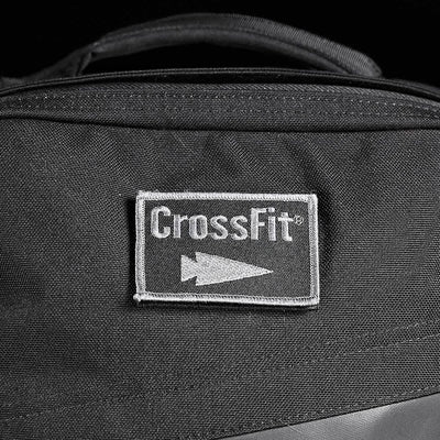 A black fabric bag prominently displays a rectangular patch embroidered with the CrossFit logo and an arrow symbol in white. The stitching accentuates the central patch, seamlessly merging durability with style, embodying the rugged design principles of GORUCK-DEMO's Patch - GORUCK x CrossFit.