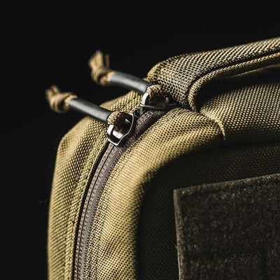 Close-up of the GR2 Field Pocket's khaki corner showcases a sturdy zipper with dual pulls. Made by GORUCK from 1000D Cordura, the textured fabric and dark background emphasize the rugged design, making it ideal as an electronics organizer.