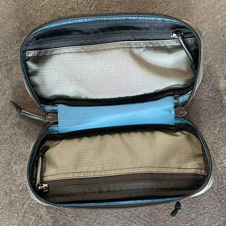 The Bullet Field Pocket Robic Nylon by GORUCK, crafted from durable Robic nylon and built by SCARS, showcases two zippered compartments—one blue and one brown—resting on a dark surface. The open pouch is empty, highlighting its inner storage sections and impressive tear strength.