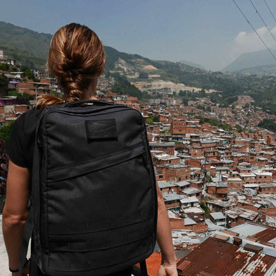 A person carrying the GR1 USA rucksack by GORUCK gazes over a densely packed hillside cityscape under a clear sky.