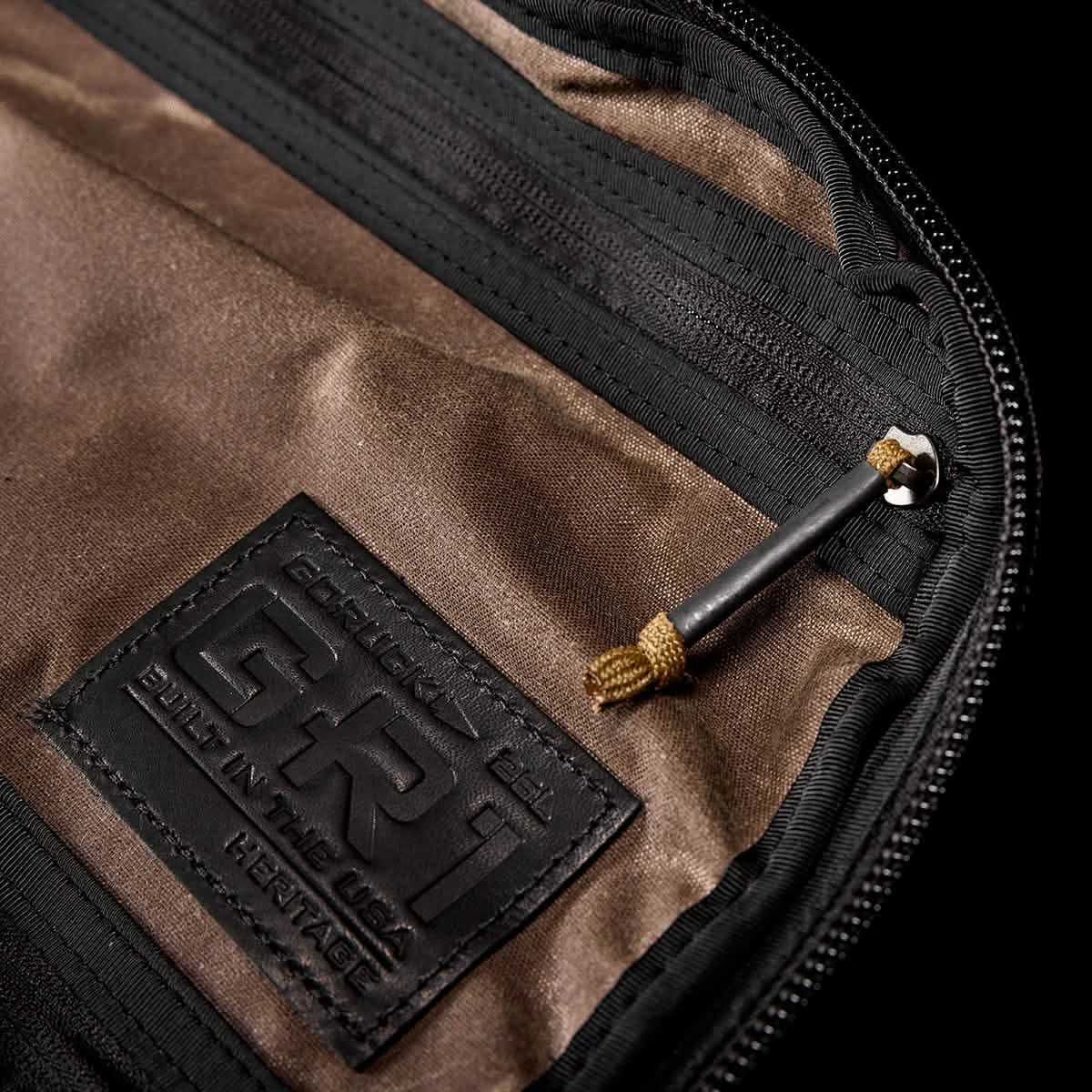Close-up of the brown and black interior of a GORUCK GR1 USA - Heritage Rucksack with a small metal tool attached by a cord. The label reads GR1 USA - Heritage, with Built in the USA beneath it. The timeless appeal of this piece complements any style, echoing the charm of its retro canvas design against a black backdrop.