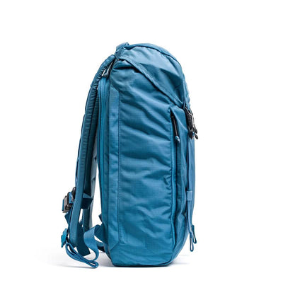 A side view of the GORUCK M23 - Ripstop ROBIC® in Seaspray and Speed Tan, standing upright, showcases its multiple zippered compartments for organization. It is designed with adjustable shoulder straps and a durable fabric texture, making it ideal for travel or outdoor use.