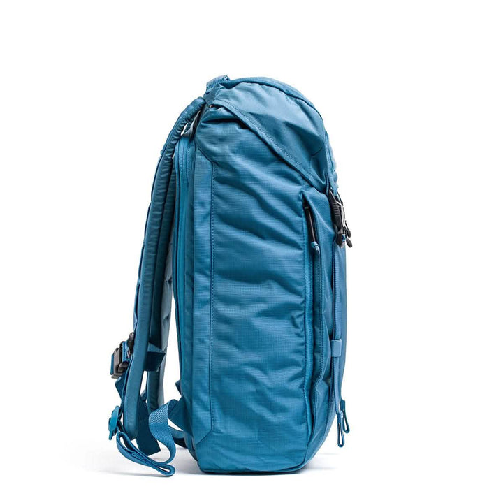 A side view of the GORUCK M23 - Ripstop ROBIC® in Seaspray and Speed Tan, standing upright, showcases its multiple zippered compartments for organization. It is designed with adjustable shoulder straps and a durable fabric texture, making it ideal for travel or outdoor use.