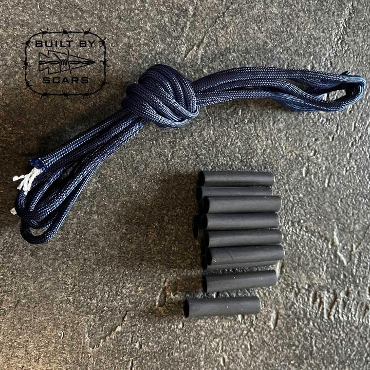 A coiled black paracord and several black cylindrical sleeves, much like heat shrink tubes, are laid out on a textured dark surface. In the top left corner is a logo featuring "BUILT BY SCARS" with a knife graphic, ideal for your next DIY ruck upgrade project.