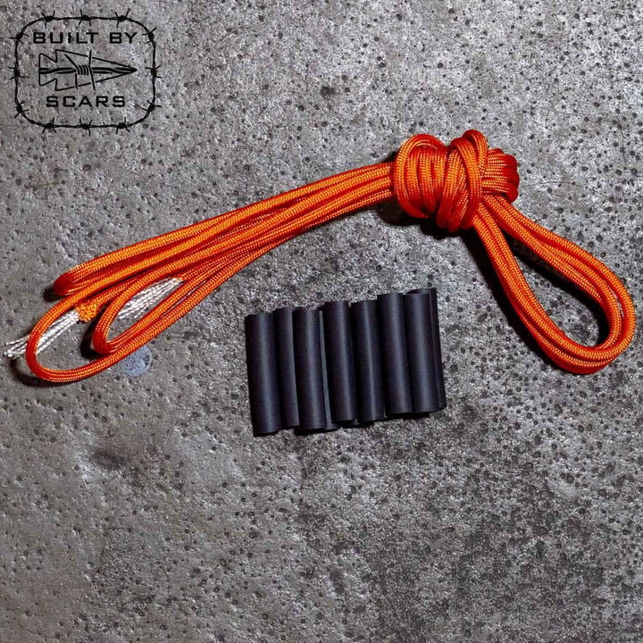 A Paracord Kit - Built By SCARS from GORUCK, featuring an orange rope with spliced loops and six black sleeves resembling heat shrink tubes, is positioned on a textured gray surface. The Built by Scars logo is prominently displayed in the top left corner, hinting at a DIY ruck upgrade.
