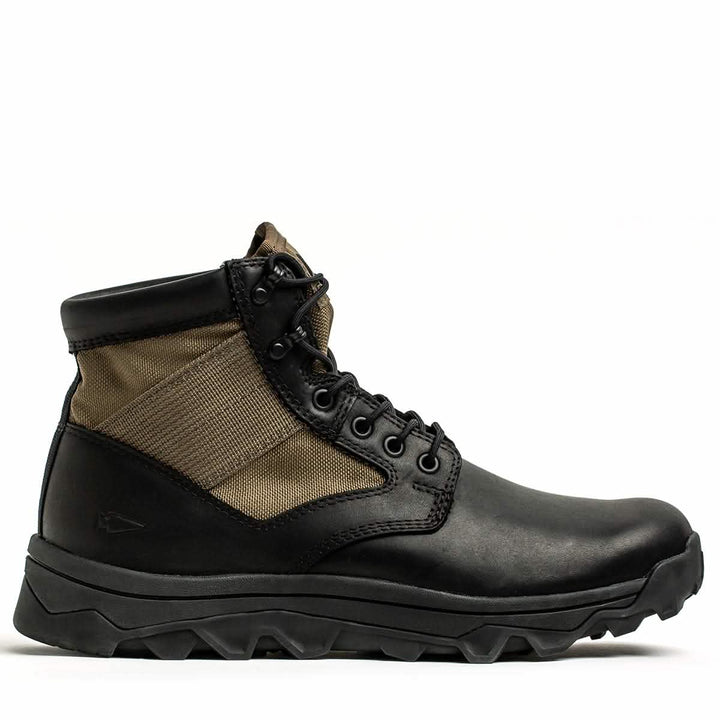 The MACV-2 - Mid Top - Origins by GORUCK is a single jungle boot crafted from black and brown leather, showcasing a rugged sole. It features metal eyelets and a lace-up design, reminiscent of the Special Forces' signature style. Its upper side includes a textured fabric section, complemented by a reinforced toe cap, all set against a plain white background.