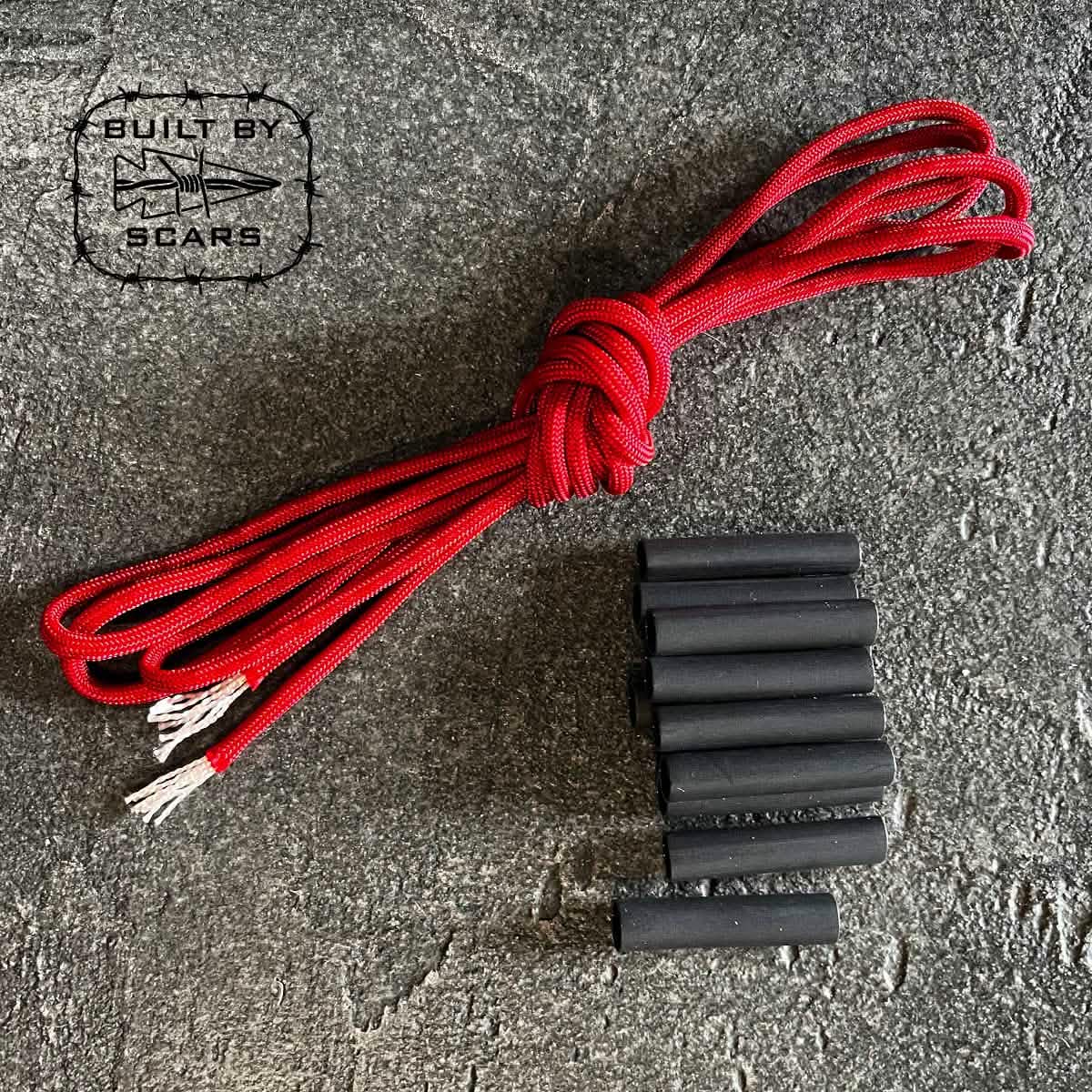 On a textured gray surface, the Paracord Kit - Built By SCARS by GORUCK is displayed, featuring a bundle of red paracord and several black heat shrink tubes, ready for your next DIY ruck upgrade. A logo in the top left corner reads Built by Scars.