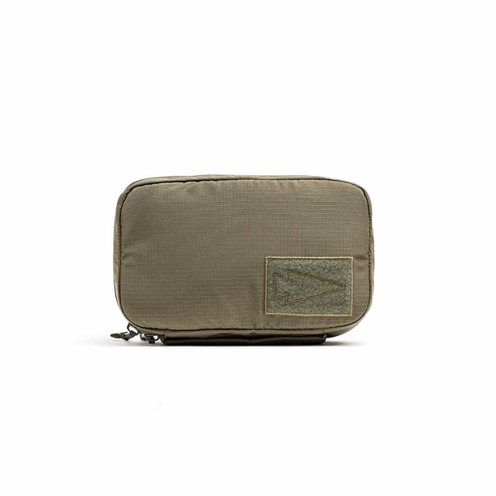 The GR1 Field Pocket - Ripstop ROBIC® by GORUCK is depicted, showcasing a khaki-colored, rectangular zippered pouch constructed from water-resistant ripstop nylon. It boasts a textured fabric and displays a patch with a triangular design on the front, making it perfect for organizing electronics. The pouch is presented against a plain white background.