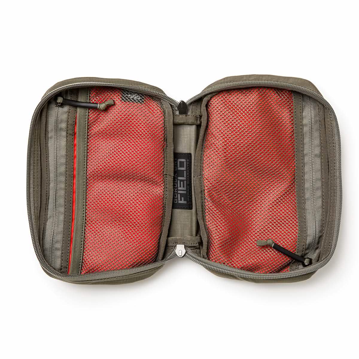 The GR1 Field Pocket - Ripstop ROBIC® by GORUCK is designed for travel, featuring a durable ripstop nylon exterior with a dual zipper closure. It includes two red mesh compartments inside to ensure items are organized securely. The gray exterior is water-resistant, and the interior label reads FIELD, making it perfect as an electronics organizer.