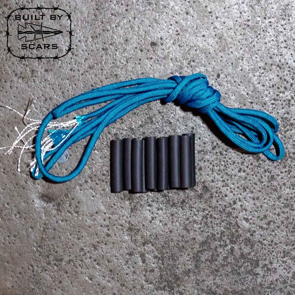 A coiled blue paracord from the GORUCK Paracord Kit - Built By SCARS lies alongside six sleek black heat shrink tubes on a textured gray surface. In the top left corner, there's a logo featuring a stylized fish with the words "Built by SCARS," perfect for enhancing your DIY rucksack projects or crafting paracord zipper pulls.