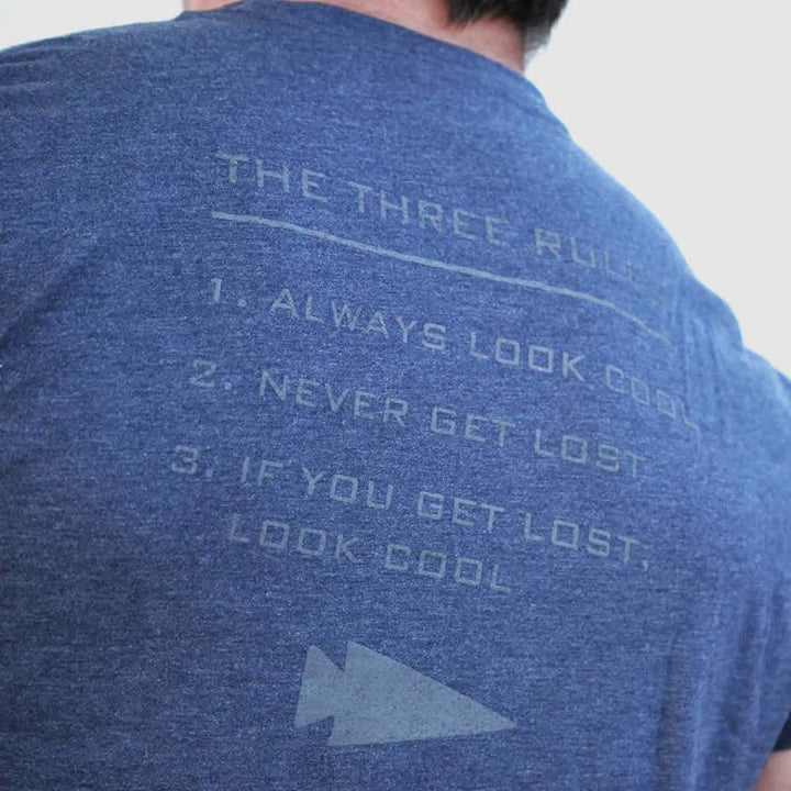 A person wearing a Three Rules Tee - Tri-Blend, semi-famous for its quirky design, displays text on the back listing three rules: 1. Always look cool, 2. Never get lost, 3. If you get lost, look cool—complete with an arrow symbol at the bottom and printed in the USA.