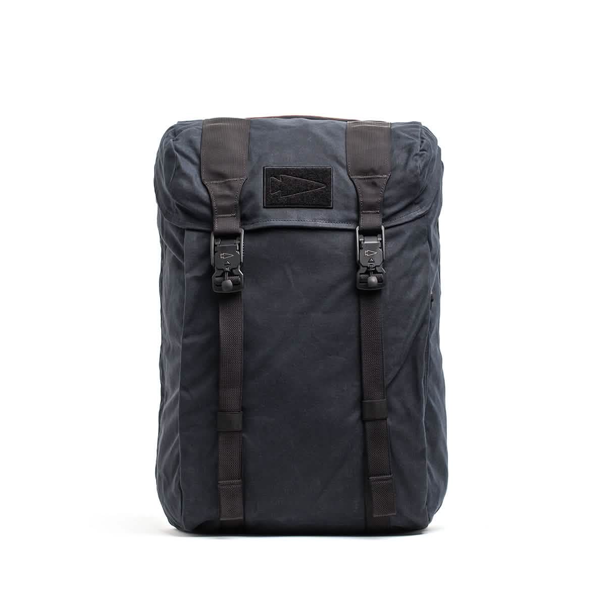Introducing the GORUCK M23 - Waxed Canvas backpack, a black rucksack boasting a simple yet rugged design. It is equipped with two front straps that have buckle closures and a top flap, crafted to meet the high standards set by GORUCK. Made from durable materials, this backpack is ideal for outdoor adventures.